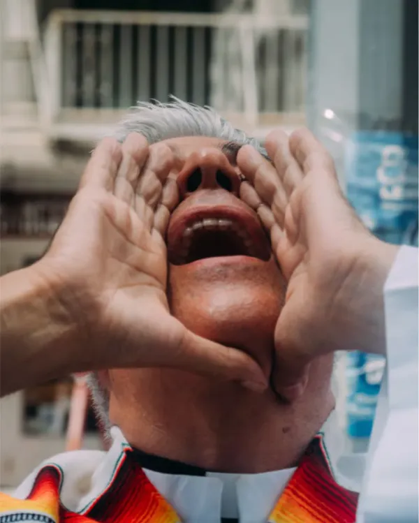 Cluse up of a man with his head back, yelling out with his hands cupped around his mouth. He is wearing a priest's collar